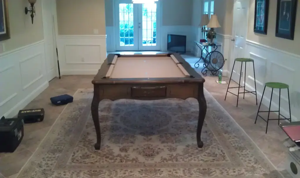 A dark wood table with cabriole legs and tan felt on a patterned rug in a white-paneled room