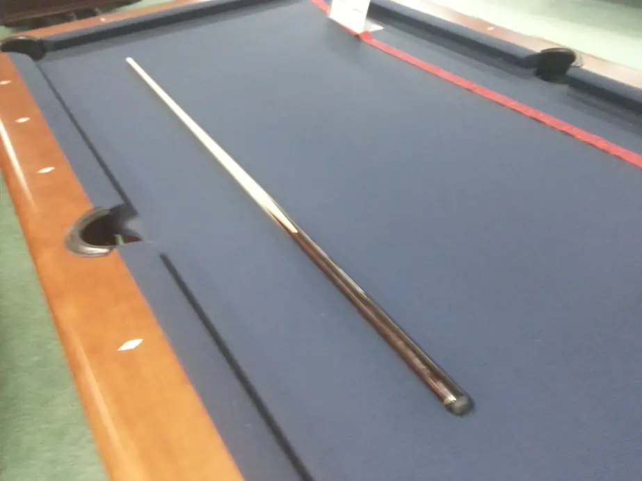 Blue felt pulled tight along a rail with a cue resting on the cloth