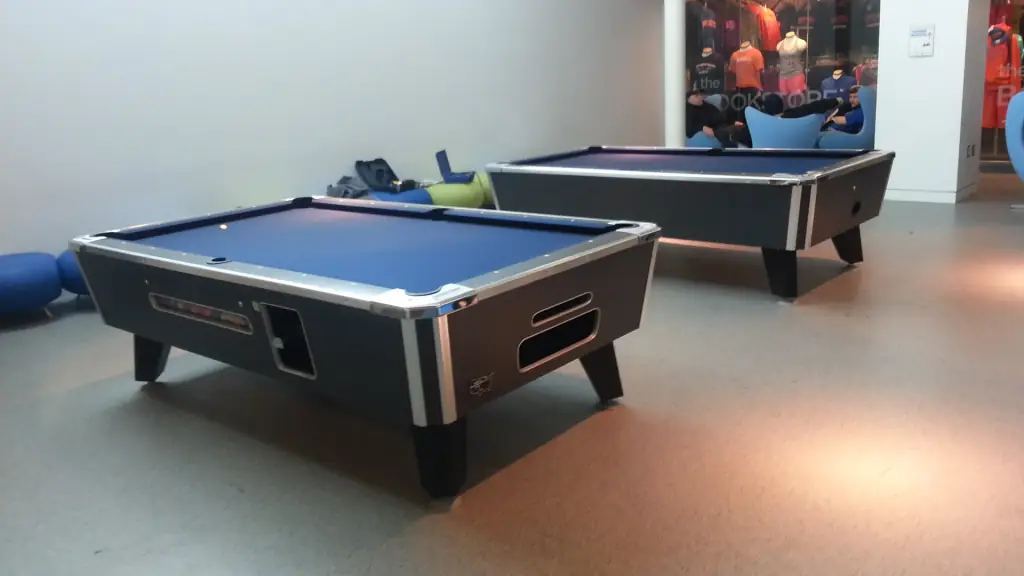 Two pool tables with blue felt, silver rails and dark tapered legs on a grey floor