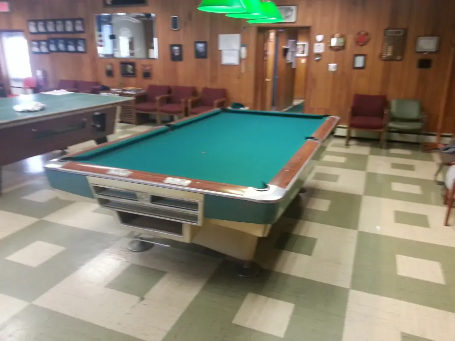 A green felt table on a checkered floor in a wood-paneled club room
