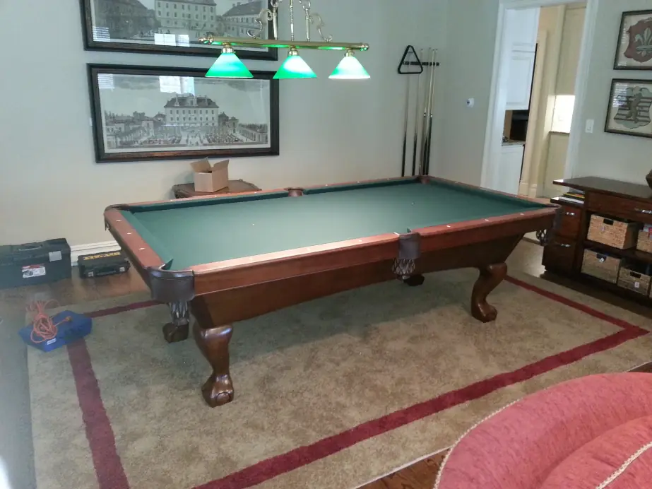 A green felt table with carved legs under three green billiard lamps