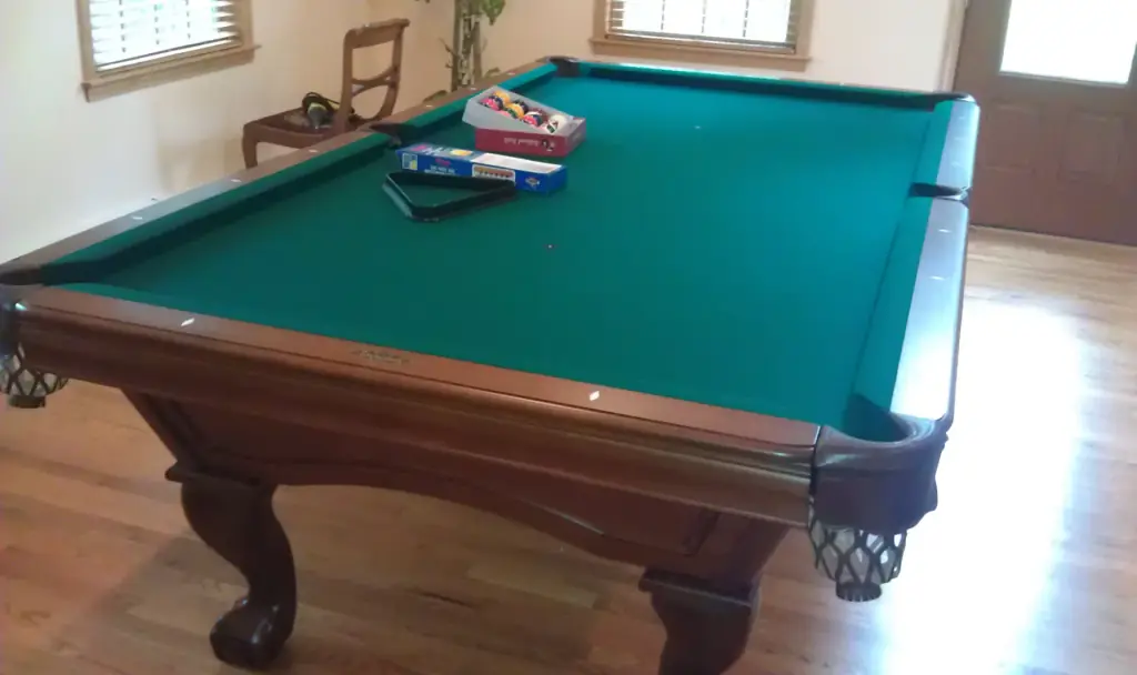 A green felt table on oak legs with a fresh set of balls on the cloth