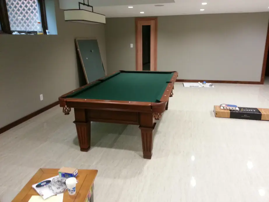 A cherry pool table in an empty grey room with boxed parts against the wall