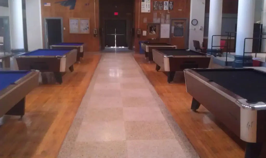 A long aisle of pool tables with blue and black felt set in a row along a terrazzo floor